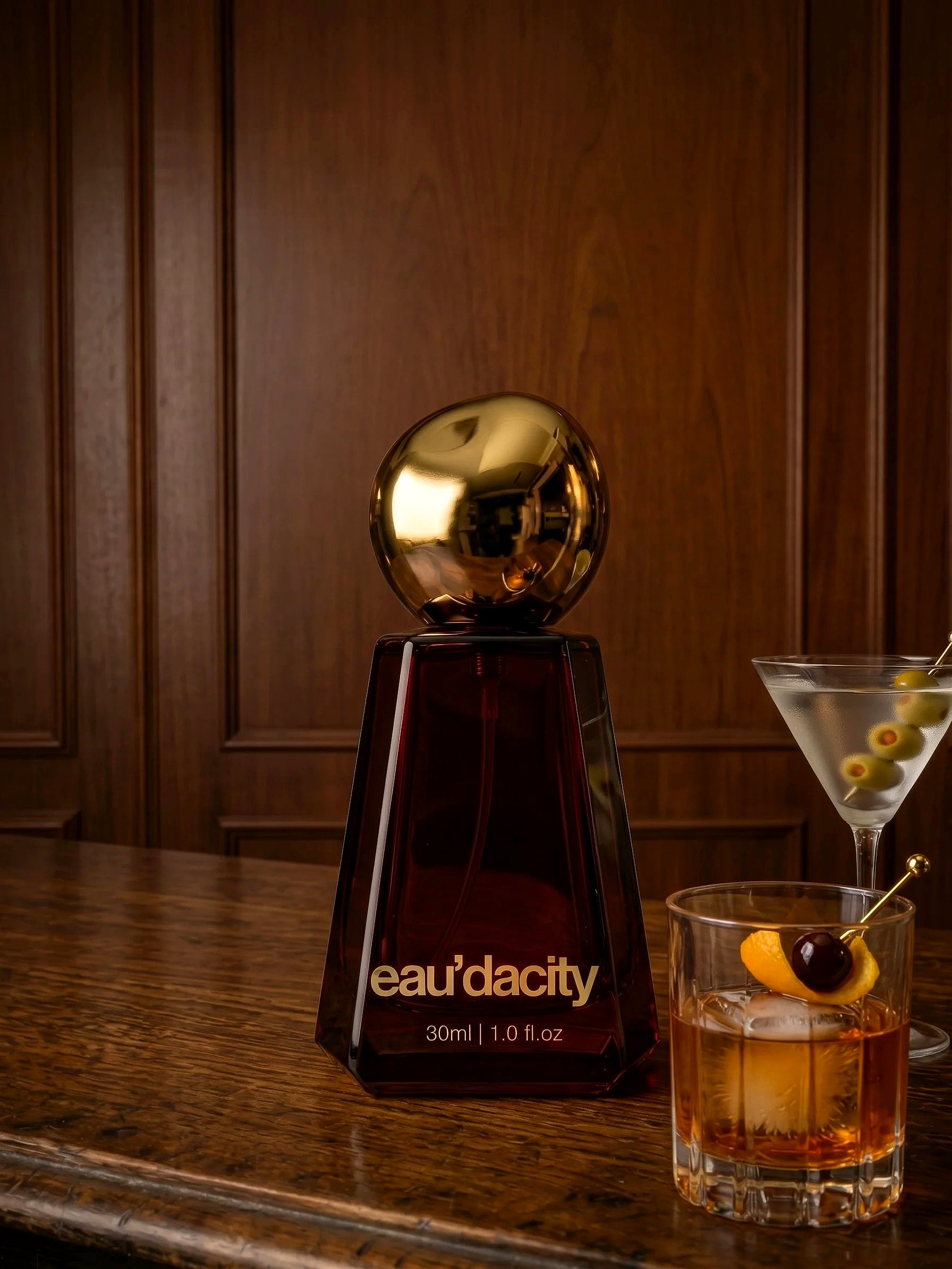 The Eau’dacity Icon bottle beside two cocktails on a wooden bar