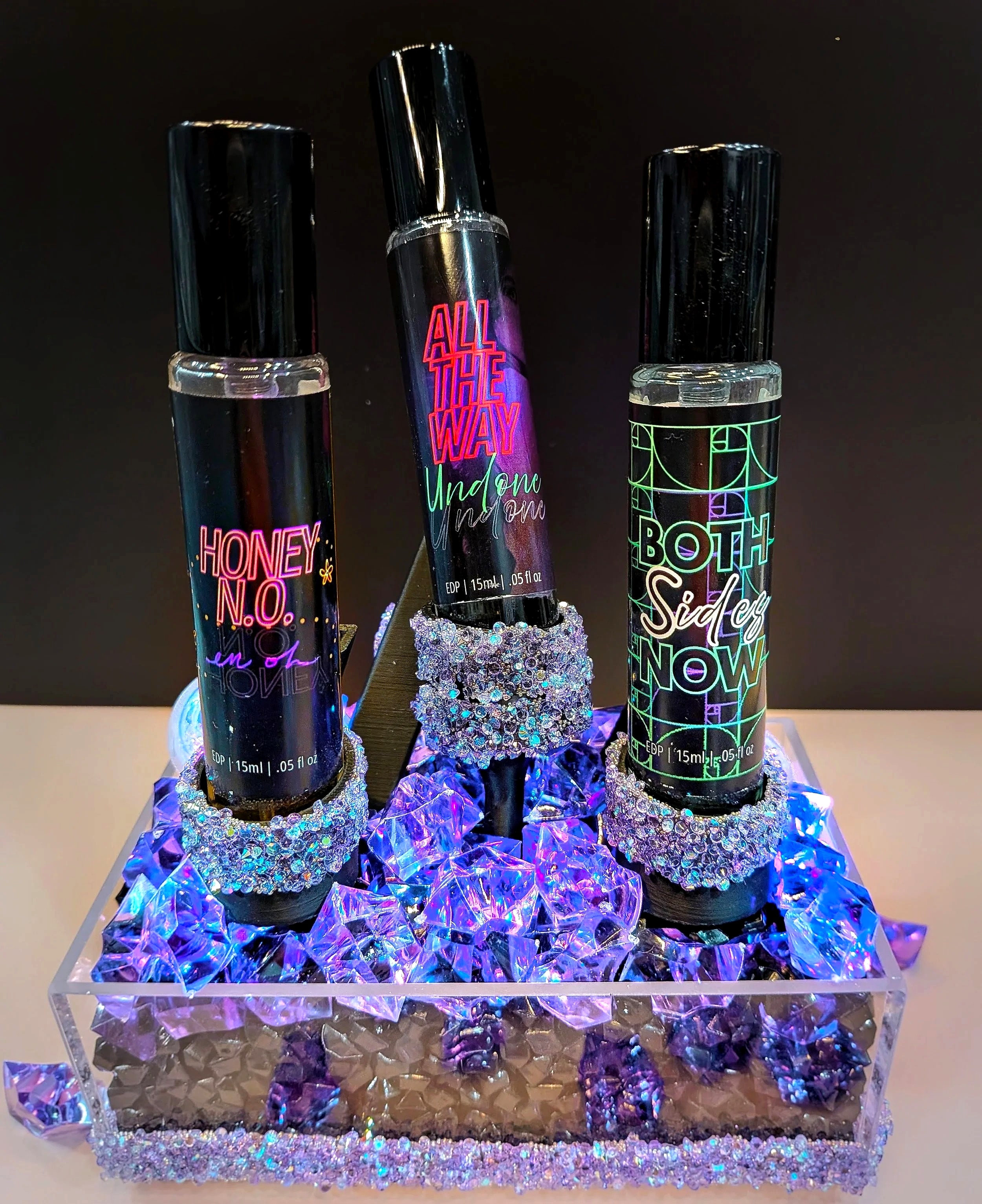 The three Love, Me perfumes on a lit stand of purple crystals